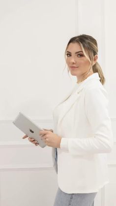 a woman standing in front of a white wall holding a tablet computer and looking at the camera