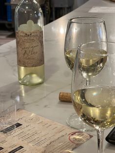 two glasses of white wine sitting on a counter top next to a bottle of wine