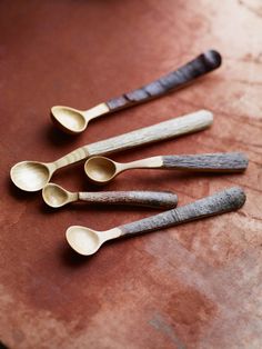 five wooden spoons lined up on top of a brown table with one empty spoon in the middle