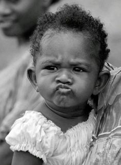 a black and white photo of a baby crying with her mother in the back ground