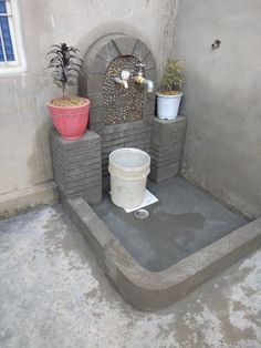 a cement fountain with buckets and plants on it in the corner of a room