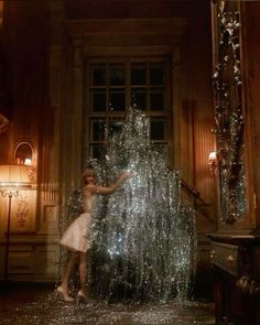 a woman standing next to a giant christmas tree in a room with lights on it