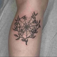 a spider web tattoo on the thigh with flowers and leaves around it in black ink