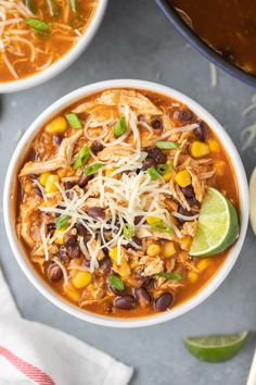 two bowls of chili chicken soup with shredded cheese and green garnish on top