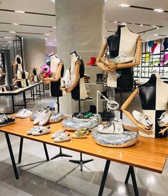 several mannequins and shoes are on display in a clothing store with wooden tables