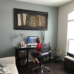 a young boy sitting at a computer desk in front of a painting on the wall