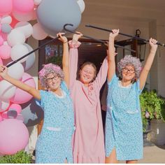 three women holding up balloons in front of a building