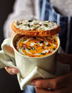 a person holding a cup filled with soup and two pies on top of it