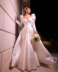 a woman standing next to a wall wearing a wedding dress