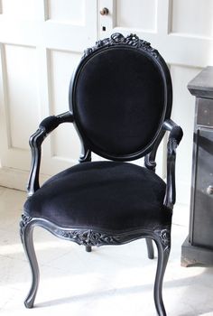 a black chair sitting on top of a white floor next to a wooden dresser and door