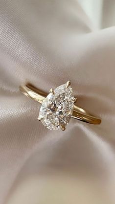 a diamond ring sitting on top of a white satin covered cloth with a gold band