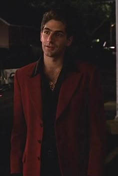 a man in a red jacket standing on the street at night with his hands in his pockets