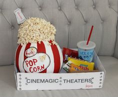 a popcorn bucket filled with movies and snacks sitting on a couch next to a cup