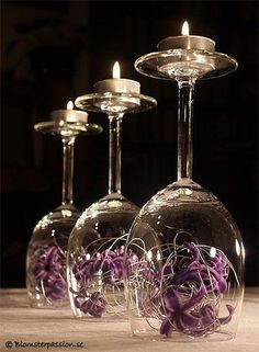 three wine glasses with purple flowers in them and one has a candle on the top