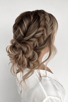 a woman with long hair wearing a white shirt and braided up into a low bun