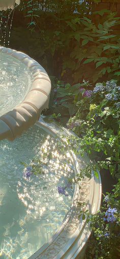 an outdoor fountain in the middle of a garden with flowers around it and water spouting from above