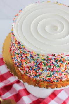 a cake with white frosting and sprinkles sitting on a checkered table cloth