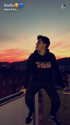 a young man sitting on top of a balcony next to a railing with the sun setting behind him