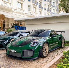 two green sports cars parked next to each other in front of a large hotel building