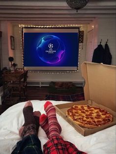 two people laying on a bed in front of a flat screen tv with a pizza