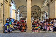 an outdoor market with people shopping and selling items on the sidewalk in front of large archways