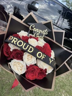 a bouquet of red and white roses in front of a graduation cap with the words proud of you on it