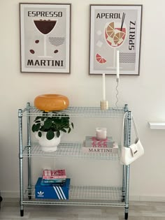 two pictures hang on the wall next to a shelf with books and a potted plant