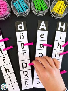 a person is writing letters with pink and green clips in front of them on a black surface