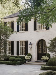 a white brick house with black shutters and large potted plants in the front yard