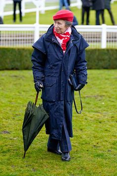 a man walking with an umbrella in his hand on the grass near some white fences