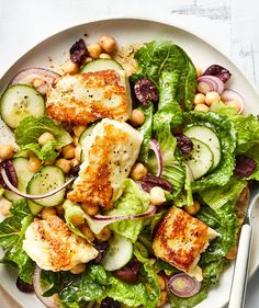 a white plate topped with salad and chicken next to a fork on top of a table