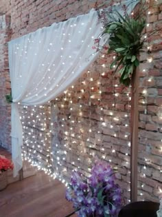 a brick wall with white lights on it and flowers in the corner next to it