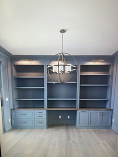 an empty room with built - in bookshelves, cabinets and a chandelier