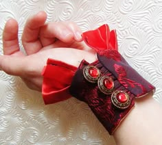 a woman's hand holding onto a red and black cuff with two rings on it