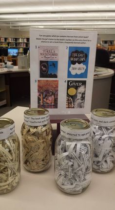 four jars filled with books on top of a white table in front of a sign