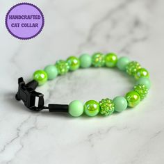 a green beaded bracelet with black clasp on a marble counter top and the words handcrafted cat collar written below it