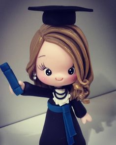 a small doll wearing a graduation cap and gown holding a blue object in her hand