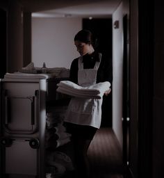 a woman in an apron is standing by the washer and looking at her folded towels