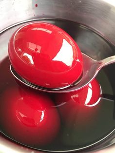 two red balls and a spoon are in a metal bowl filled with black liquid,