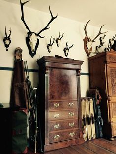 several deer heads are mounted on the wall above an antique dresser and other items in a room