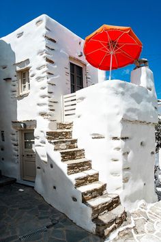 an orange umbrella sitting on the side of a white building with stone steps and stairs