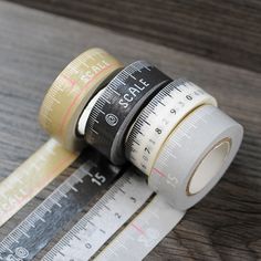 two rolls of tape sitting next to each other on top of a wooden table with measuring tape