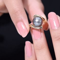 a woman's hand holding a ring with a gray pearl on top of it