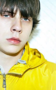 a young man wearing a yellow jacket and looking at the camera with an intense look on his face