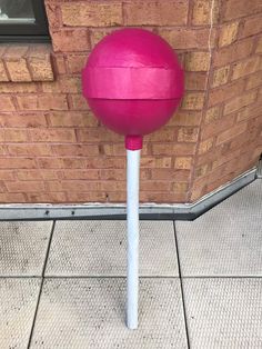 a large pink ball sitting on top of a white pole next to a brick wall