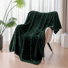 a green blanket sitting on top of a chair next to a potted plant