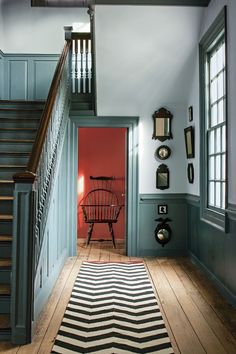 a hallway with blue walls and wooden floors has a striped rug on the hardwood floor