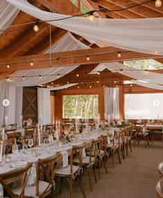 an indoor wedding reception with white draping and wooden tables set up for dinner