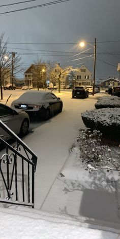 cars are parked on the street in front of houses covered with snow at night time