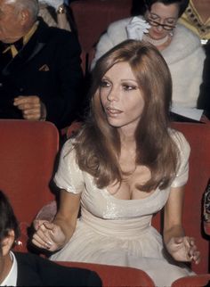 a woman in a white dress sitting on a red chair with her hands folded out